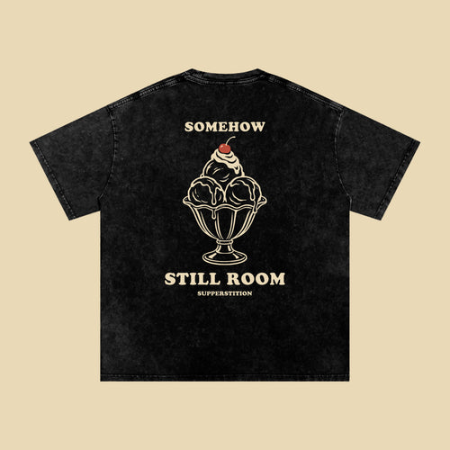 Back of the washed black Somehow, Still Room tee: an ice cream sundae in a glass dish with a cherry on top, between the words SOMEHOW and STILL ROOM.